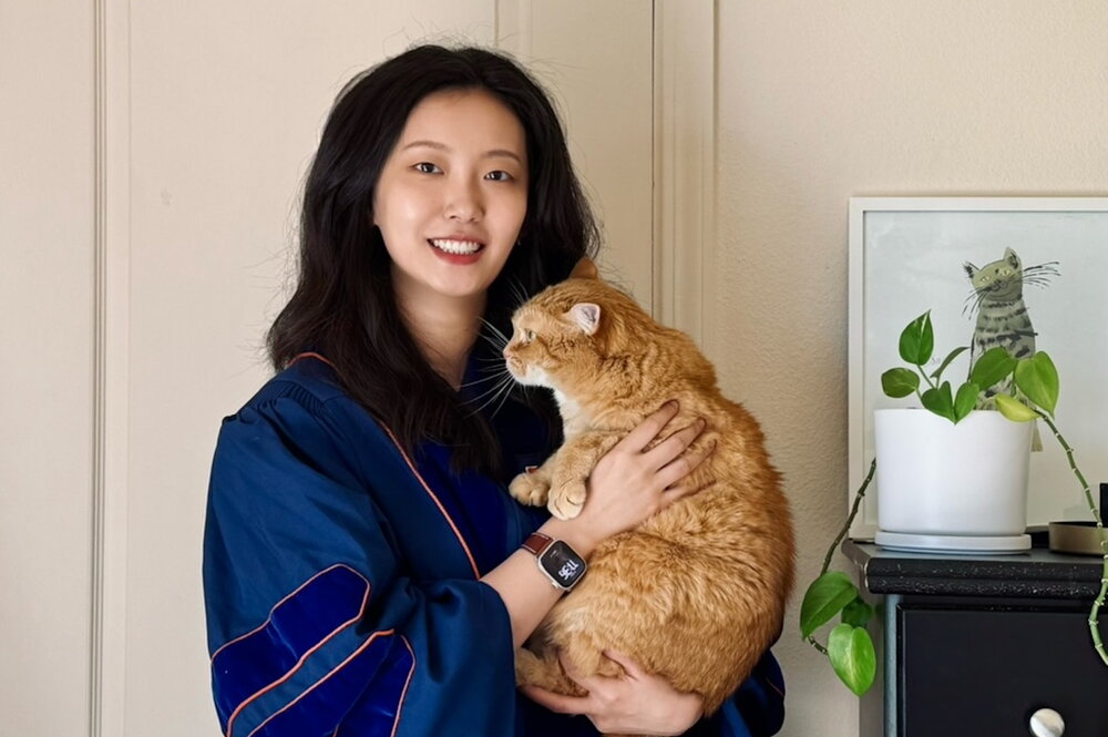Dr. Yu wearing her doctoral graduation robe and holding an orange cat