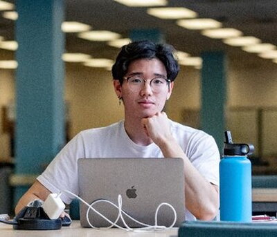 Student sitting in undergraduate library looking up from is laptop and resting his head on his fist